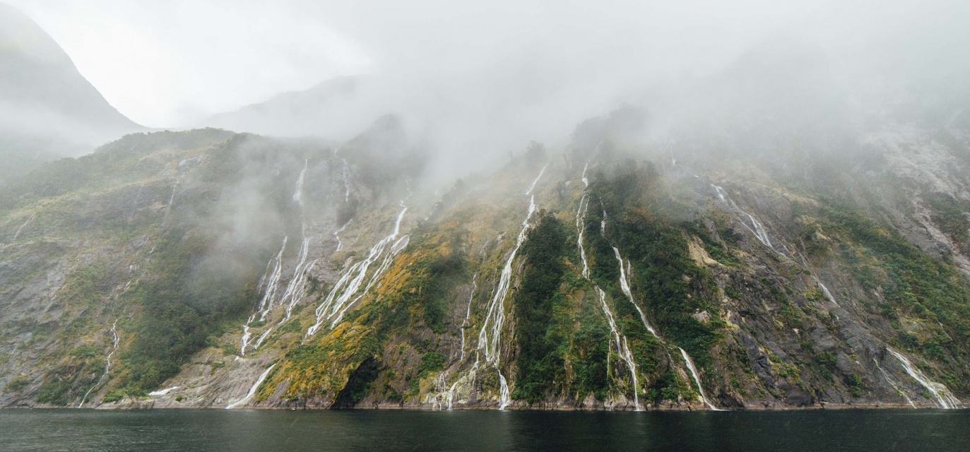 Low cloud parting reveals beautiful waterfalls and trees on the cliffs at Piopiotahi / MIlford Sound