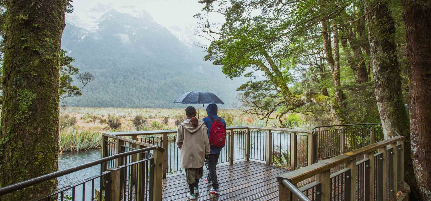 A couple enjoy a rainy stroll on the boardwalk at Mirror Lakes on the Milford Road